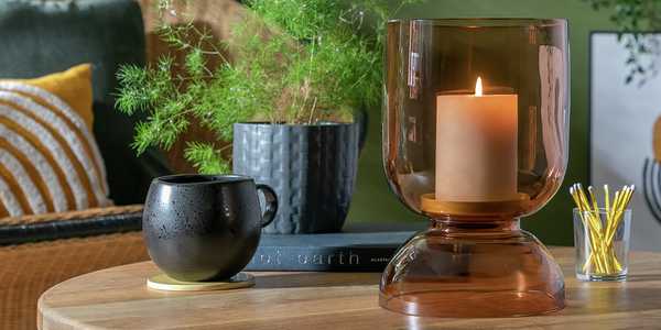 A cup, indoor plant and a candle in a candle holder on a table.